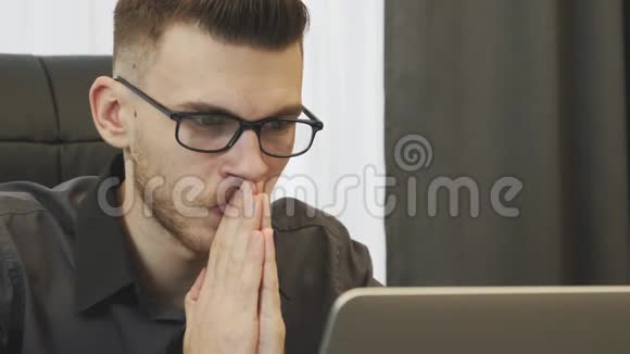 有希望的人看着笔记本电脑屏幕的肖像商人祈祷看电脑屏幕近距离观看年轻男性的脸视频的预览图