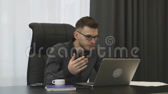 年轻自信的男性在办公室里看笔记本电脑屏幕穿灰色西装戴眼镜的白种人坐在办公桌前工作视频的预览图