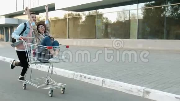 快乐的男人推着购物车兴奋的女孩坐在城里玩视频的预览图