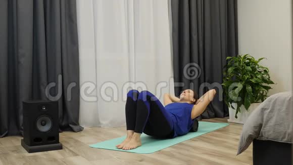 女孩在客厅里做运动女性按摩脊柱肌肉使用滚筒瑜伽健身教练做康复训练视频的预览图