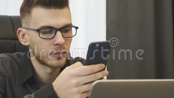 接近自信的男人看智能手机屏幕成功的商人坐在办公桌前打电话年轻视频的预览图