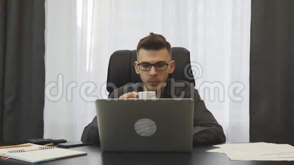成功的商人在他的现代办公室喝咖啡穿西装的年轻人在工作场所喝咖啡坐着的男经纪人视频的预览图