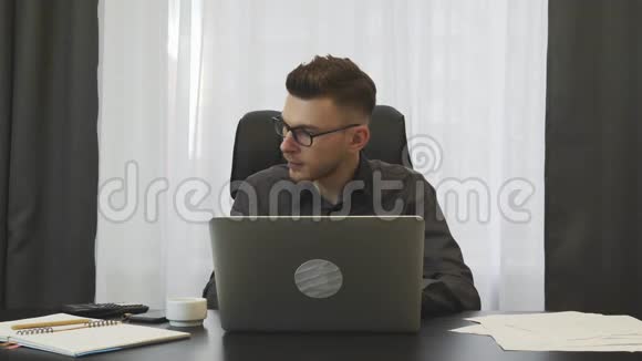 经纪人在办公室工作年轻的成功商人在办公室里用笔记本电脑工作男人在笔记本上记笔记坐在他的屁股上视频的预览图