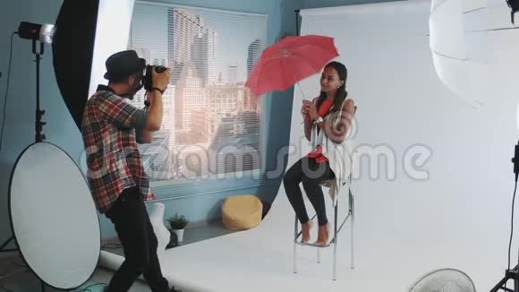 时尚的非洲模特在酒吧的高椅上摆着红色的雨伞拍照视频的预览图
