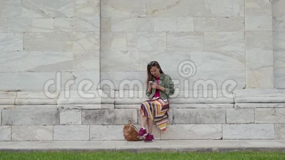 意大利广场上著名地标CampoSanto的大理石墙上坐着一个漂亮的女孩她用手机坐着视频的预览图