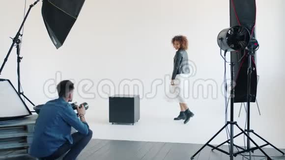 一位漂亮的混血女士和摄影师一起在摄影棚里摆镜头跳跃的姿势视频的预览图