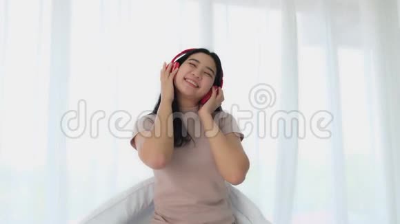美丽的亚洲年轻女性在床上用无线耳机听音乐摇头晃脑视频的预览图