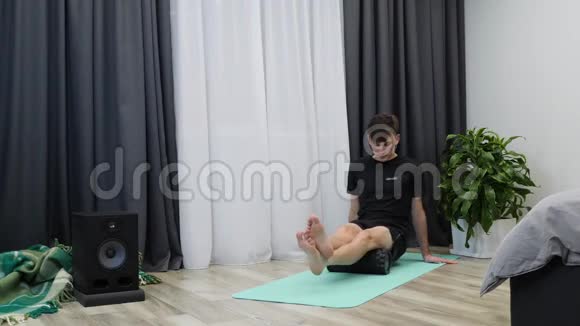 人在起居室做运动男孩按摩臀部肌肉使用滚筒瑜伽健身教练做复健运动视频的预览图