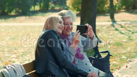 秋天在一个美丽的公园里年轻年老的女人在智能手机上自拍的变焦镜头视频的预览图