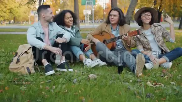 在城市公园的草坪上不受欢迎的学生在弹吉他视频的预览图