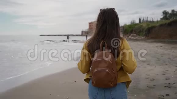 旅游女孩带着棕色背包在春天沿着地中海海滩散步后视图视频的预览图