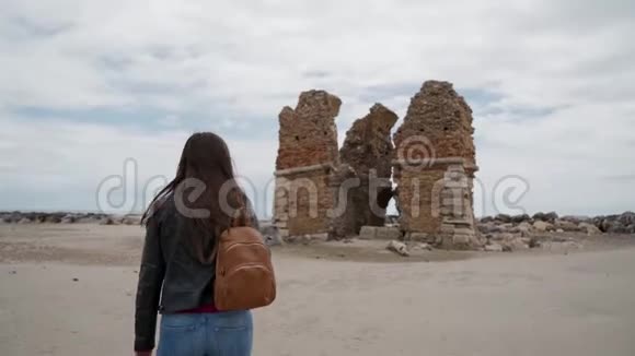 意大利拉迪斯波里一座古老要塞托里弗拉维亚的废墟旁一个带背包的长发黑发女孩后视图视频的预览图