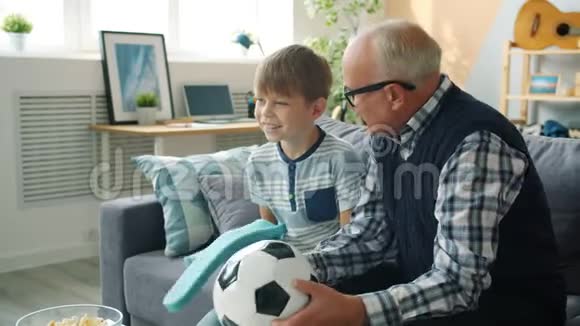 欢乐的家庭祖父和孙子在电视上欢呼拥抱着看足球视频的预览图