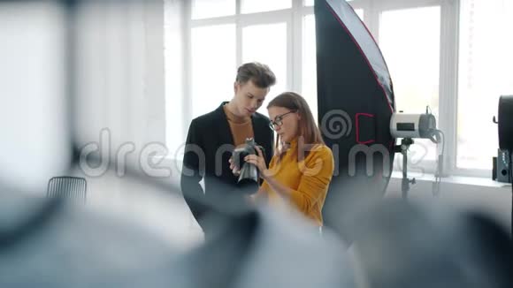 女孩和男孩模特在照相馆聊天看数码相机的照片视频的预览图