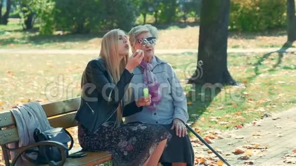 在公园里和祖母坐在一起吹泡泡的快乐年轻女子中弹视频的预览图
