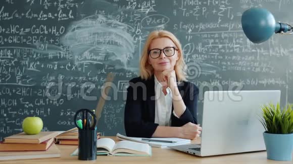快乐的女老师微笑着用黑板墙看着课桌上的摄像机视频的预览图