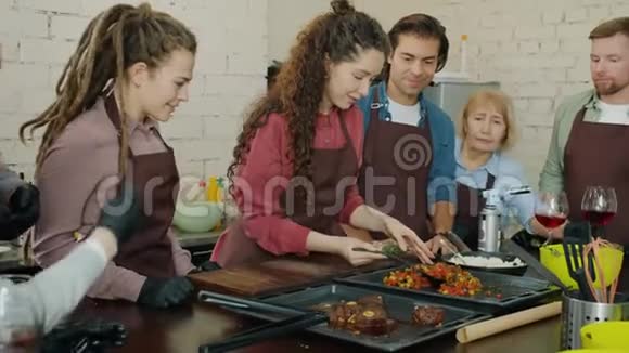 快乐的年轻女子在厨房里和一群烹饪班的学生一起做饭视频的预览图