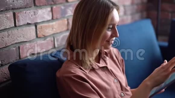 年轻快乐的女人用数字平板电脑坐在客厅舒适的沙发上视频的预览图