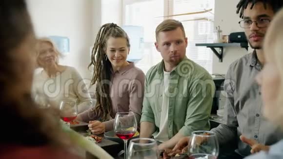 快乐的人们谈笑风生地坐在餐桌上一边吃东西一边喝饮料一边玩视频的预览图