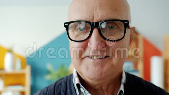 一位戴眼镜微笑着在家看相机的老人的特写照片视频的预览图