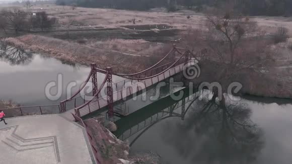 年轻的女孩正在公园里用河和桥跑步女运动员在人行桥上跑步女性在娱乐场所慢跑视频的预览图