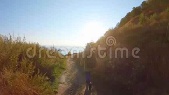 带着背包的女孩正在日落时沿着通往大海的路走视频的预览图