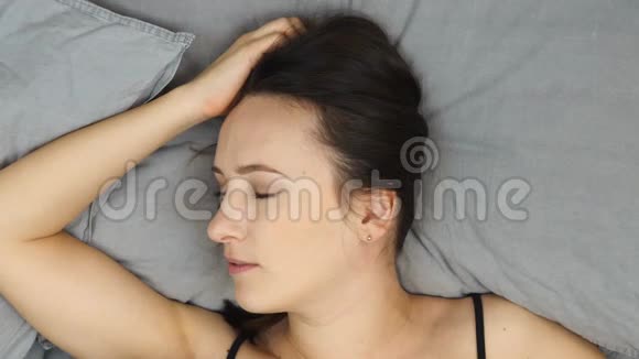 女人躺在铺着灰色毯子的床上微笑着看着摄像机俯视图年轻害羞的女性用毛毯遮住脸视频的预览图