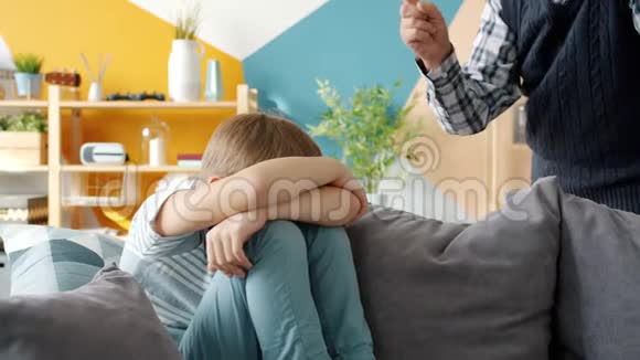 严厉的祖父惩罚小男孩对坐在沙发上哭泣的孩子摇着手指视频的预览图