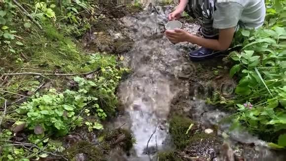一个男孩徒步旅行者徒步旅行者用金属旅游杯从山泉中获得清澈的淡水视频的预览图