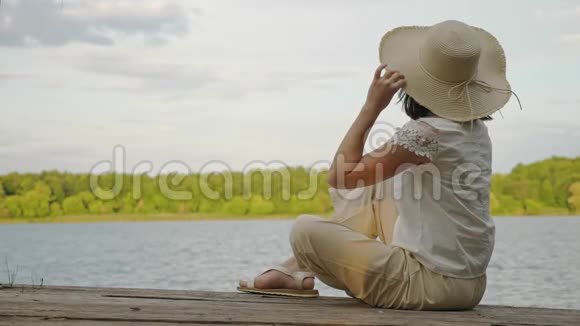 女人坐在一个古老的木制码头码头的边缘视频的预览图