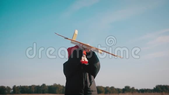 快乐的小男孩在日落时在大自然中玩木飞机孩子拿着一架木飞机梦想成为一个视频的预览图
