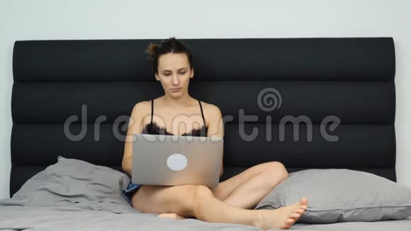 成年女孩在网上在笔记本上聊天年轻女子坐在床上用笔记本电脑看屏幕和打字视频的预览图