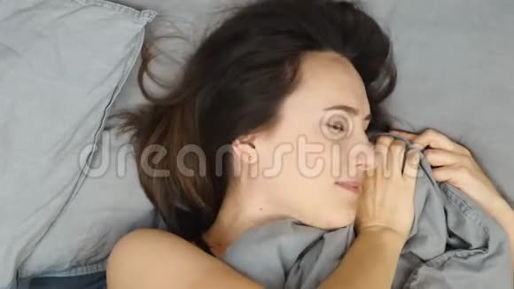 深色头发的女性躺在被毯子覆盖的床上肖像迷人的女人躺在床上微笑着看着摄像机视频的预览图