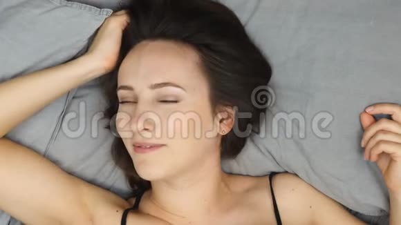 穿内衣的女人躺在床上用毯子盖住她的脸年轻的黑发女孩躺在床上微笑着看着相机视频的预览图