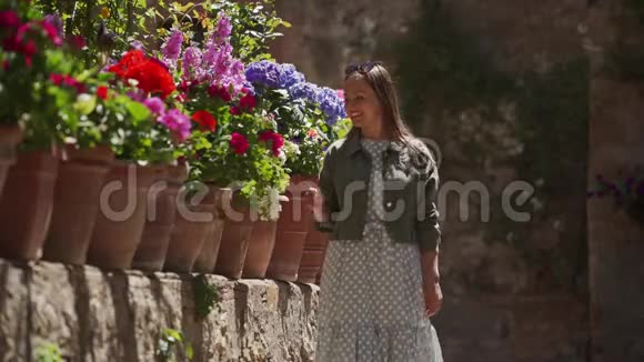 快乐的女孩穿着浪漫的裙子夹克沿着花坛漫步抚摸着花朵视频的预览图