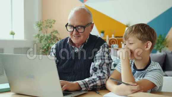退休爷爷和快乐孙子用笔记本电脑在家里谈笑风生视频的预览图