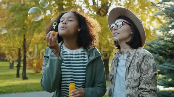 阳光明媚的秋日快乐的年轻女性朋友在公园里吹肥皂泡视频的预览图