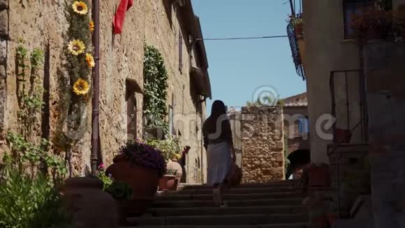 穿着浪漫裙子的女孩穿过皮恩扎老城舒适的街道后视图视频的预览图
