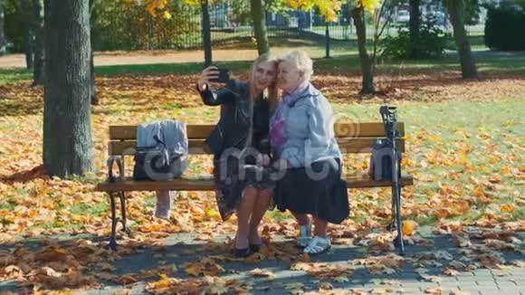 秋天在一个美丽的公园里年轻年老的女人在智能手机上自拍的变焦镜头视频的预览图