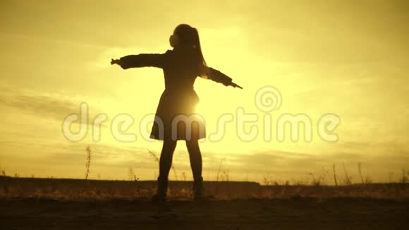 剪影女孩站在田野里在日落时张开双臂童年梦想的概念视频的预览图