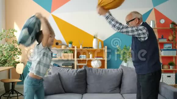 家庭幸福的慢动作老人和男孩笑着打枕头视频的预览图