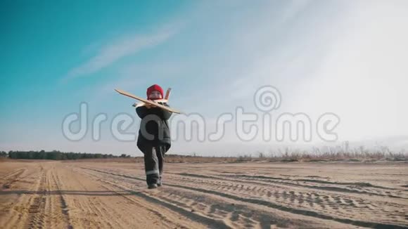 快乐的小男孩在日落时在大自然中玩木飞机孩子拿着一架木飞机梦想成为一个视频的预览图