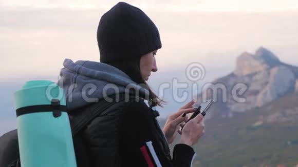 年轻女孩旅行者背包使用智能手机数字设备模糊山顶背景触摸显示视频的预览图