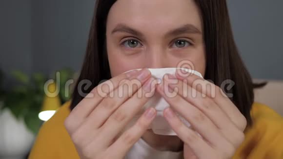 女孩吹鼻子有魅力的白种人女人用手帕吹鼻子看镜头感冒流感流涕视频的预览图