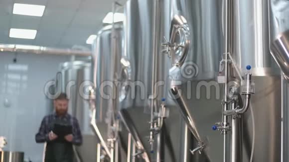 一个穿着带胡须的围裙的男性啤酒师来到啤酒罐写下读数手工艺啤酒生产视频的预览图