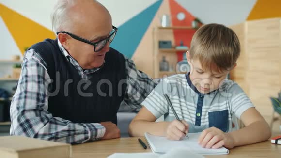 聪明的小学生在公寓里和祖父做作业时动作缓慢视频的预览图