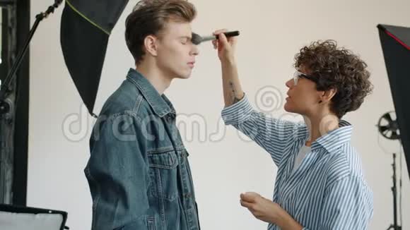 化妆师在摄影前在照相馆男模特的脸上涂化妆品视频的预览图
