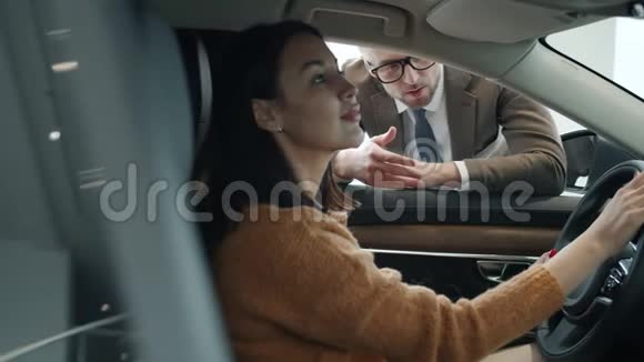 坐在新车里的汽车陈列室的销售代表说漂亮的女士视频的预览图