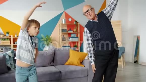 退休的祖父和可爱的孩子在家里一起做体育锻炼视频的预览图