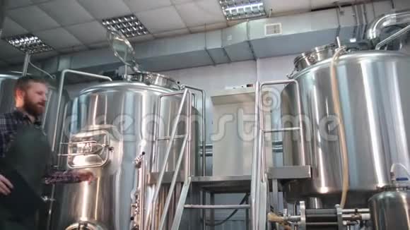 一个穿着带胡须的围裙的男酿酒师看着啤酒罐里面并控制着酿造过程视频的预览图